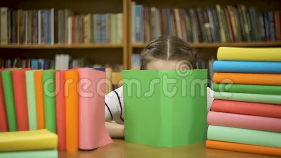 一个女学生躲在图书馆的一本书后面视频的预览图