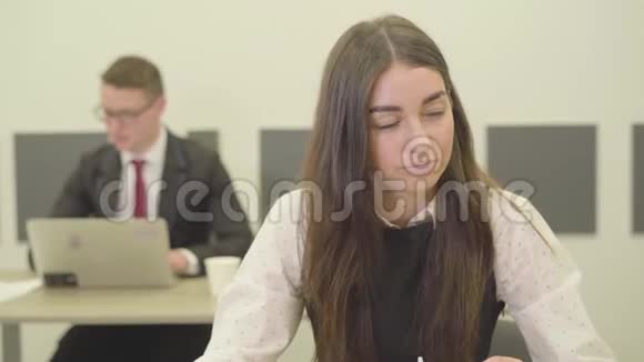 一位穿着正式服装的可爱体贴的年轻女士坐在办公室的前台而她的男同事则坐在办公室视频的预览图