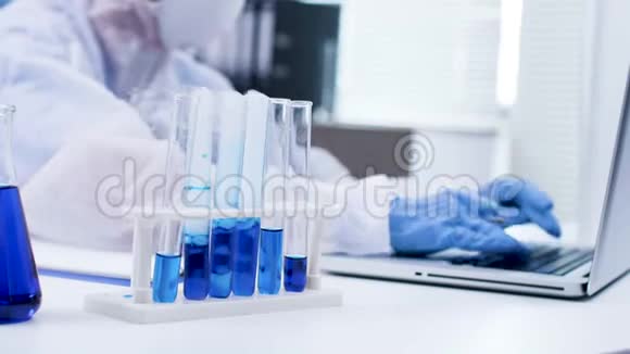 关闭科学家在她的笔记本电脑上打字和在试管中吸烟的蓝色液体视频的预览图