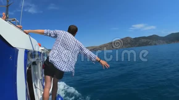 一个英俊的年轻人站在船上或游艇上漂浮在海里暑假和朋友一起慢动作视频的预览图