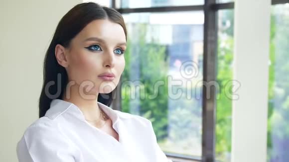 可爱的年轻女子一双漂亮的蓝眼睛站在办公室的窗户旁视频的预览图