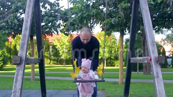 爸爸和他可爱的小女儿站在秋叶秋千附近妈妈来了带来了美丽的黄叶视频的预览图