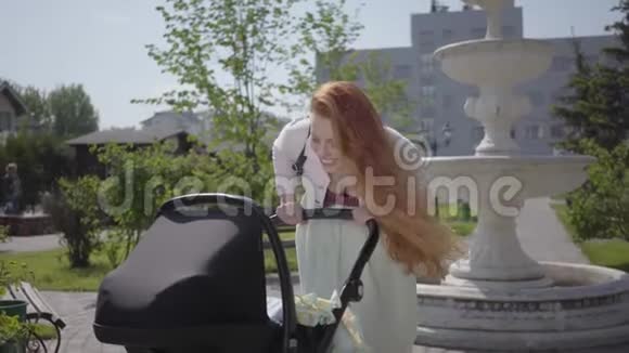 可爱的红发妈妈弯下腰在公园里笑着可爱的女人和她的孩子一起享受阳光明媚的一天视频的预览图