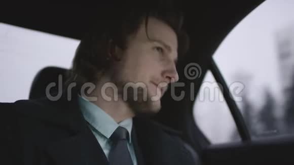 英俊的男子棕色头发穿着开心果衬衫灰色外套坐在车里看着他的手表付着钱视频的预览图