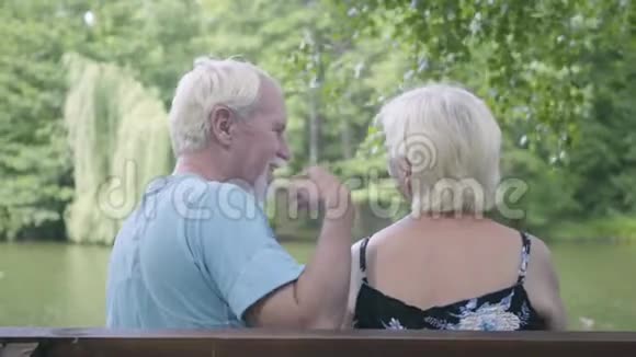 一对幸福成熟的夫妇坐在河边的长凳上欣赏大自然拥抱妻子的男人视频的预览图