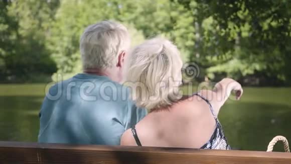 一对幸福成熟的夫妇坐在河边的长凳上欣赏大自然用手指指着别处视频的预览图