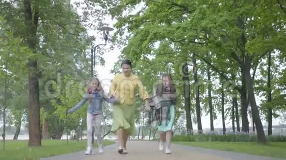 一个成熟优雅的女人牵着两个孙女在公园里跑步祖母与视频的预览图