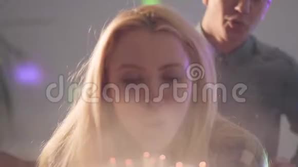 金发女孩吹灭蛋糕上的蜡烛年轻人站在她身后女人有生日庆典视频的预览图