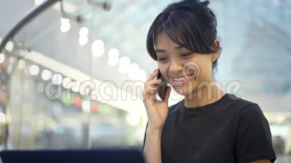 年轻的亚洲女性带着笔记本电脑微笑着在电话中交谈的肖像视频的预览图