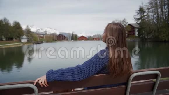 年轻的女人坐在一张木凳上在阳光明媚的春天里湖光山色令人惊叹妇女视频的预览图