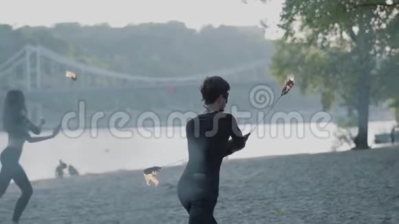 穿着黑色衣服的职业男子和妇女站在河岸边用火焰表演节目熟练的射击技巧视频的预览图
