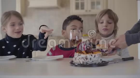 三个孩子在桌子上拿着小蛋糕和果汁眼镜女人的手切蛋糕给男孩放一块盘子视频的预览图