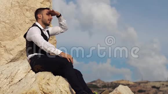 英俊时尚的家伙坐在岩石上同龄人进入远处塞浦路斯帕福斯视频的预览图
