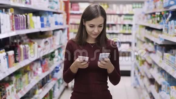 年轻女子在超市的两种产品中选择看着相机微笑视频的预览图