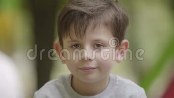 可爱的微笑男孩看着坐在户外的相机的肖像无忧无虑的童年一个小孩在为摄像机摆姿势视频的预览图