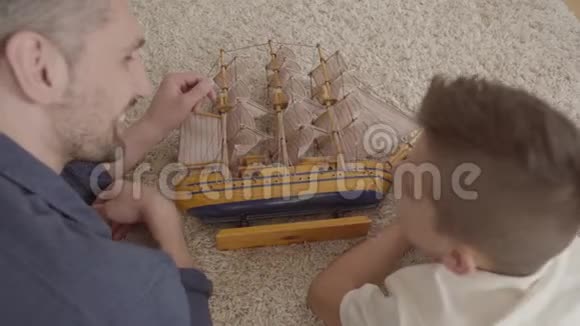 肖像可爱的父亲和儿子躺在地上毛茸茸的地毯上玩船模特写镜头视频的预览图