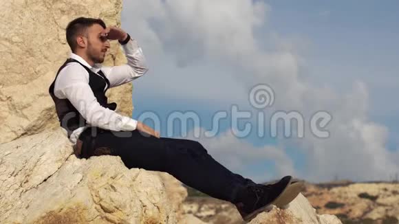 英俊时尚的男人穿着华丽的布坐在海边的岩石上塞浦路斯帕福斯视频的预览图