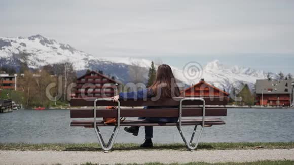 年轻的女人坐在一张木凳上在湖和山上看到了令人惊叹的景色而且很放松享受风景如画的女人视频的预览图