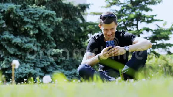 快乐男人在草地上的城市公园里放松时用手机聊天视频的预览图