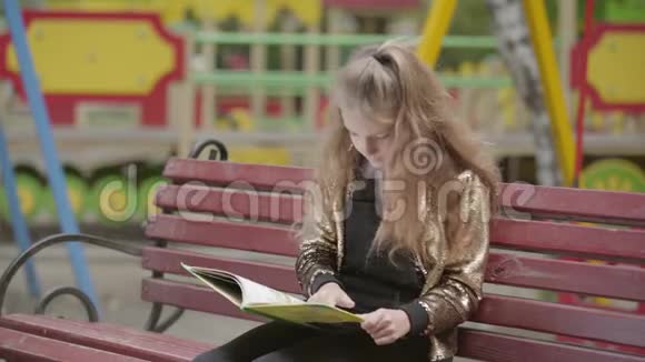 可爱的少女正在户外坐在长凳上看书视频的预览图