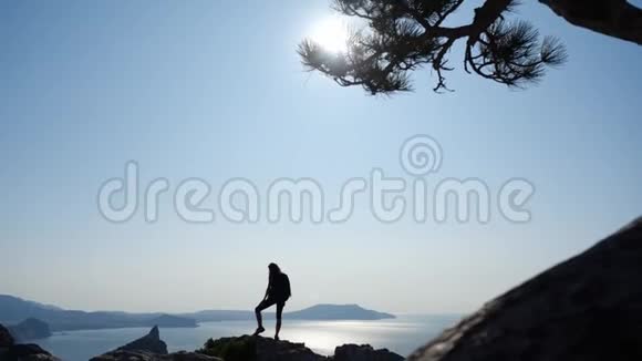 一个年轻有灵感的女人的剪影她背着背包双手举起来站在海面上的山顶上视频的预览图