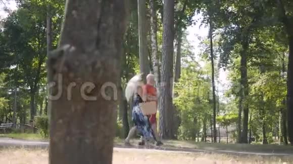快乐的成熟夫妇一起在公园散步优雅的高级女人拿着阳伞老人和女人花时间视频的预览图