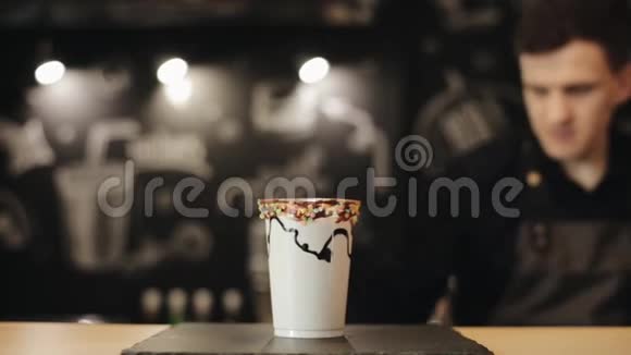 一位咖啡师把一个甜甜圈放在奶昔上放在塑料杯里用鲜奶油装饰视频的预览图