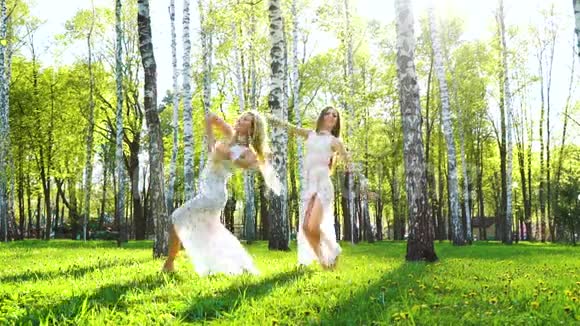 阳光照耀着两个穿着性感礼服的年轻女人在桦树林跳舞视频的预览图