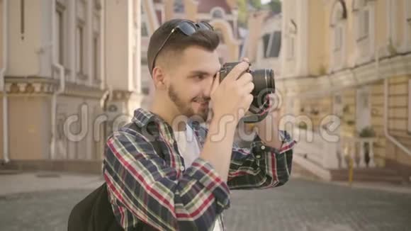 年轻的新手留胡子的摄影师在一个古老城市的街道上拍照那里有美丽的建筑旅游费用视频的预览图