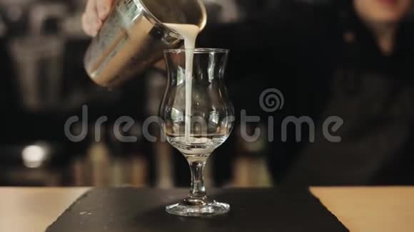 将金属摇床上的冷奶昔倒入酒吧柜台上的空玻璃杯中视频的预览图