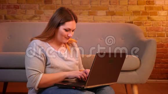 漂亮的超重女商人坐在地板上微笑着在笔记本电脑上打字对在舒适的家里工作感到满意视频的预览图