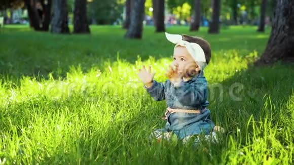 可爱的小女孩穿着牛仔裤发带坐在阳光明媚的公园里绿草如茵视频的预览图