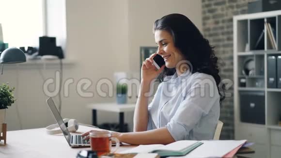 快乐的女员工在手机上说着笑在办公室里用笔记本电脑视频的预览图