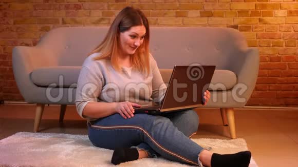 此外尺寸模型坐在地板上在笔记本电脑上的视频聊天在舒适的家庭氛围中体贴和快乐视频的预览图