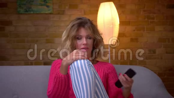 穿着粉红色毛衣的轻松家庭主妇的特写镜头在舒适的家中用心看电影视频的预览图