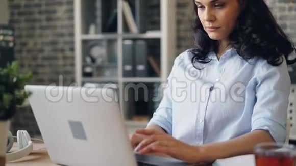 疲惫的年轻女士用笔记本电脑打字和在工作场所打哈欠的肖像视频的预览图