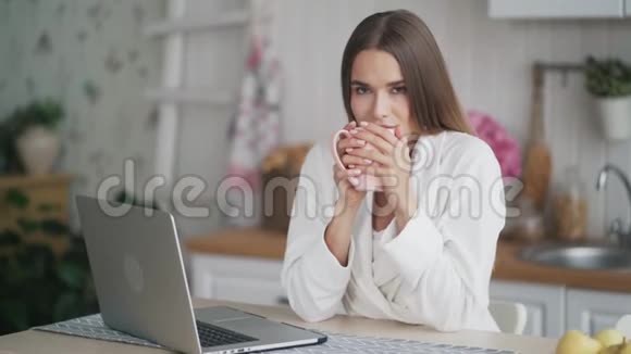 美丽的微笑女人在厨房喝咖啡看着镜头视频的预览图
