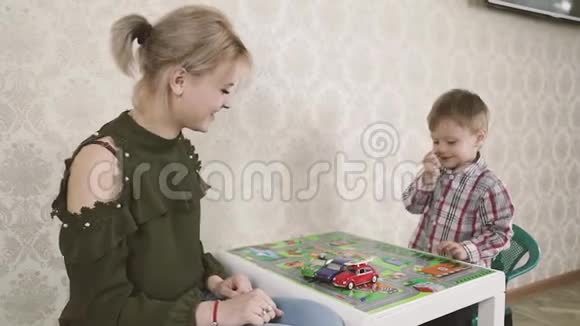 微笑的女人儿童心理学家和男孩在孩子们桌子上玩五颜六色的汽车视频的预览图