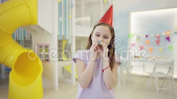 快乐的女孩在镜头前戴着锥帽吹着生日哨子视频的预览图