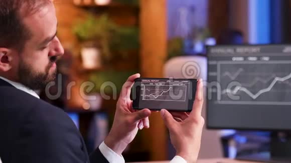 穿西装的企业家看着手机上的图表的肩膀镜头视频的预览图