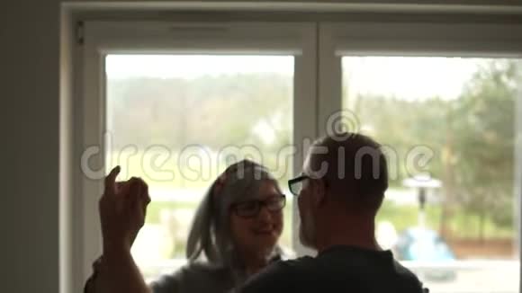 可爱的成熟夫妇在家窗前跳舞丈夫和妻子庆祝结婚纪念日视频的预览图