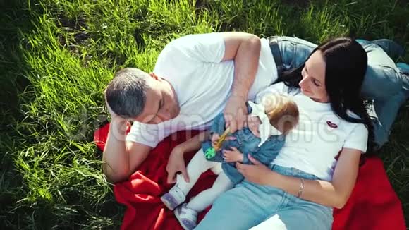 相机旋转在家庭上方女婴在夏日花园的毯子上放松视频的预览图
