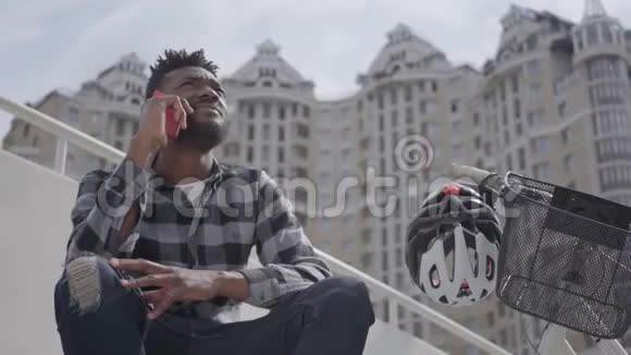 肖像可爱英俊的非裔美国人坐在他的自行车附近的城市建筑背景那个家伙视频的预览图