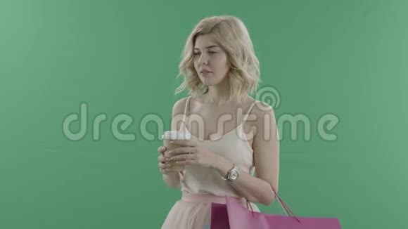 有魅力的女人拿着袋子一边喝咖啡一边在绿色屏幕上等人视频的预览图