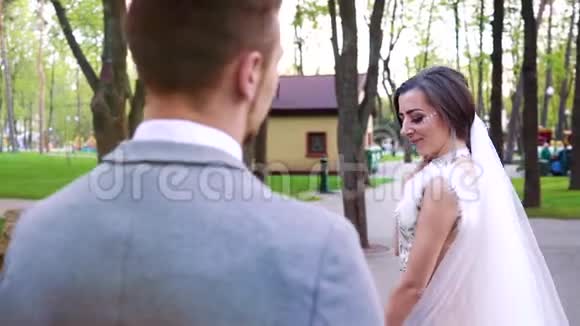 美丽的新娘微笑着在阳光明媚的公园里站着新郎走来走去视频的预览图