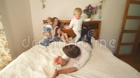 淘气的家庭孩子和妈妈一起爬上父亲的床手持射击视频的预览图