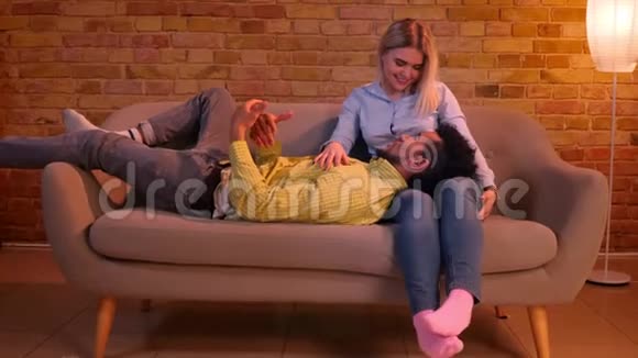 非洲男人躺在他的白种人女朋友的腿上在家庭气氛中愉快地交谈视频的预览图