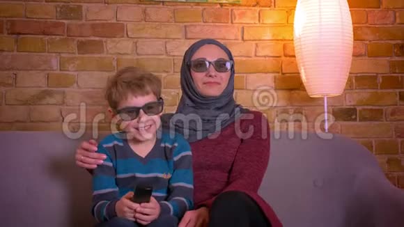 小男孩和他的穆斯林母亲戴着头巾戴着3D眼镜在家看喜剧时大笑的肖像视频的预览图