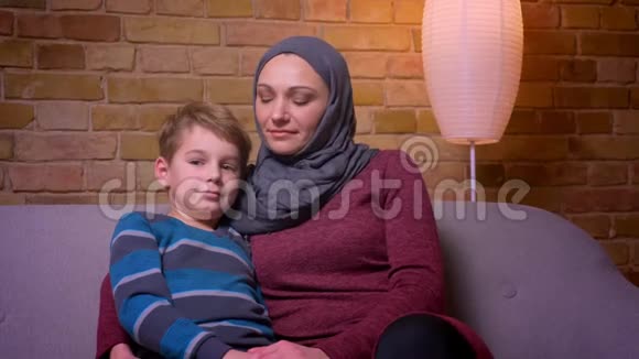 特写镜头中小男孩和他的穆斯林母亲戴着头巾微笑着进入镜头在家里互相倾斜着头视频的预览图