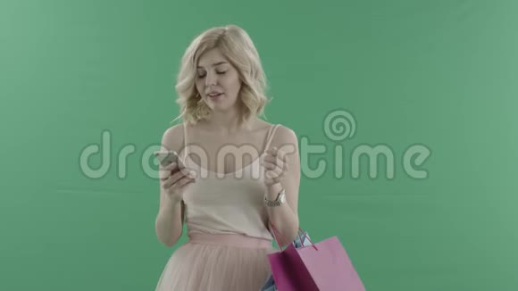 年轻漂亮的金发女郎带着包在智能手机上对着绿色屏幕打电话视频的预览图